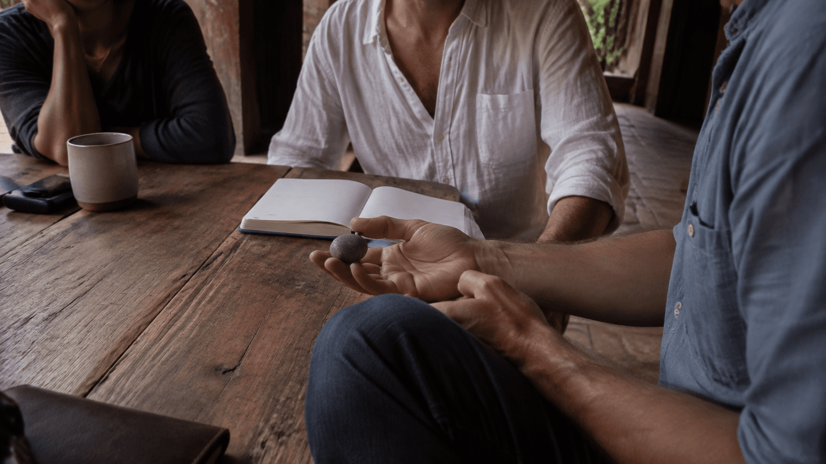 Un grupo conversando alrededor de una mesa de madera, con una piedra en la mano