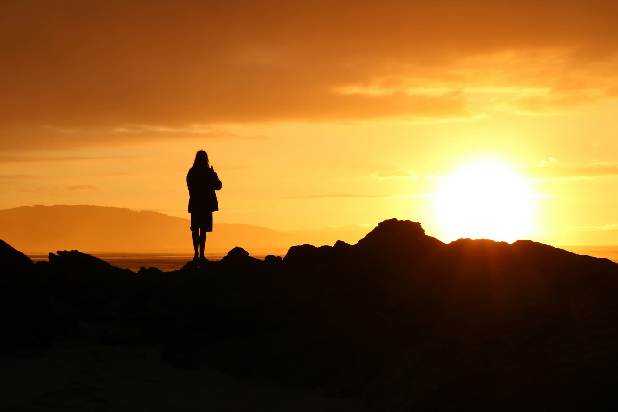 Una persona de pie en silueta sobre las rocas, observando el atardecer